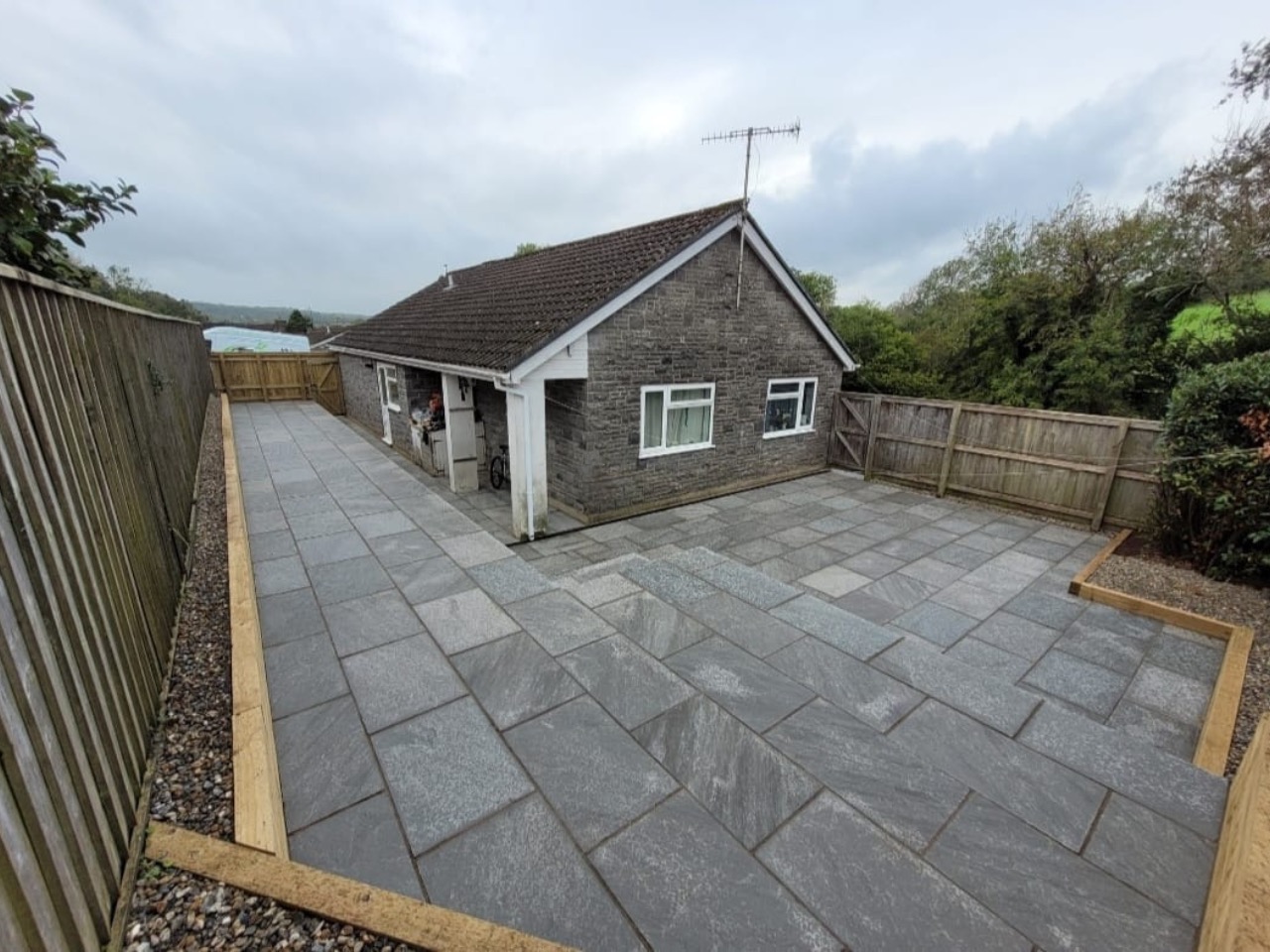 Large grey porcelain patio with sleeper edging at a bungalow